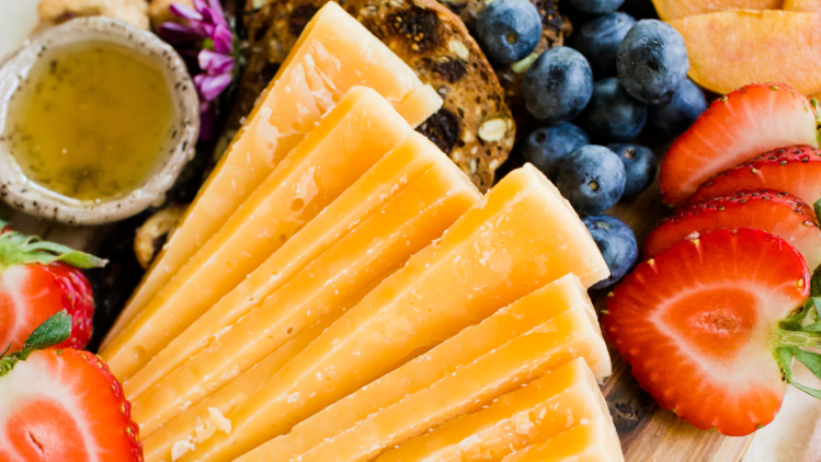 A close‑up view of an artisan cheeseboard featuring neatly arranged wedges of aged gouda surrounded by fresh strawberries, blueberries, crisp crackers, and a small bowl of honey.
